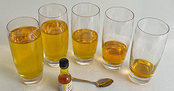Glasses in a line filled with different amounts of liquid and a tea spoon