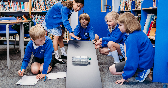 children in the classroom observing a bottle rolling down a sloped board