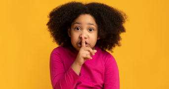 a child placing her finger to her mouth to symbolise the need to be quiet