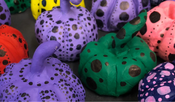 a close up image of small, colourfully painted pumpkins, decorated with various sizes of black dots