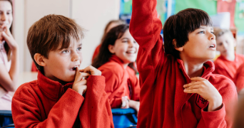 primary children engaged in their classroom lessons, with one child having their hand raised