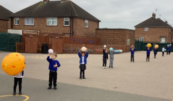 Primary school children standing in a line outdoors, each holding a model of a planet to represent the solar system