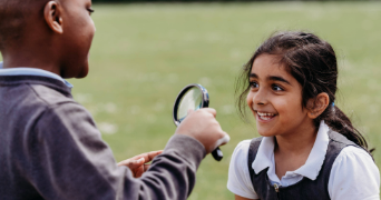 Children using magnifying glasses outdoors during a primary science activity, observing and discussing findings together