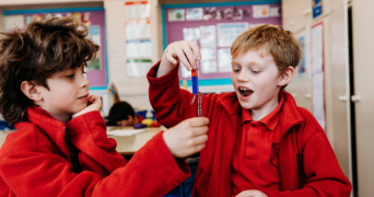 Two primary school children investigating magnetism using magnets and paperclips in a classroom.