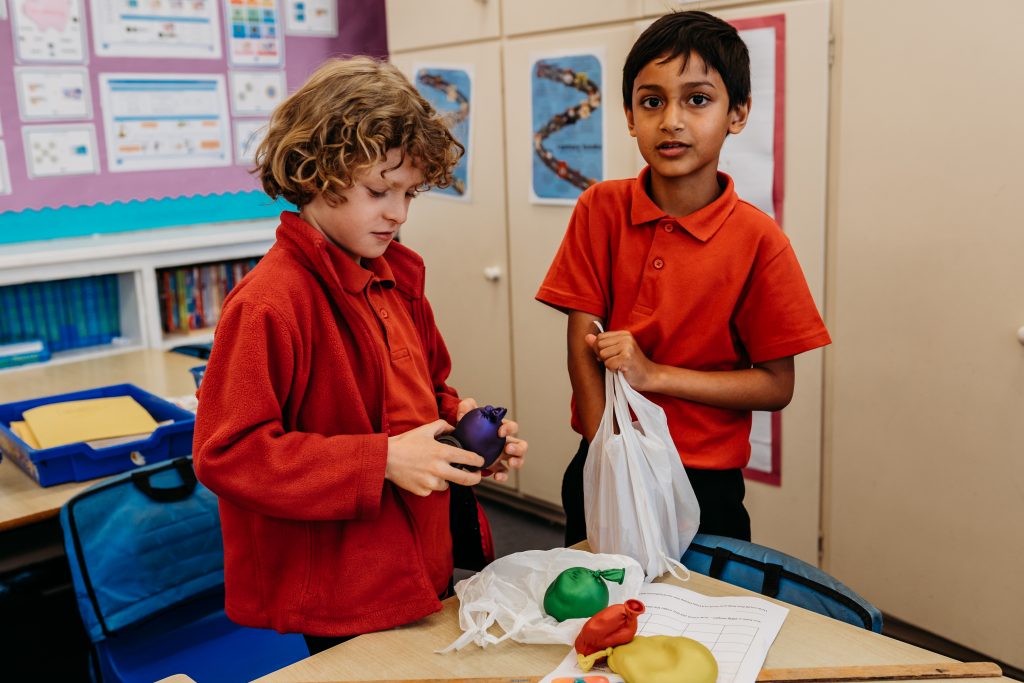 two children in classroom feeling balloons filled with different materials